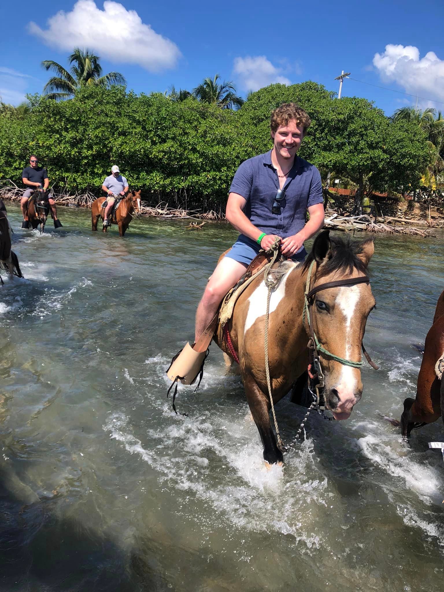 Riders on horseback entering shallow Caribbean water